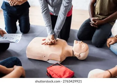 A group of delegates kneeling around a CPR manikin while chest compressions are demonstrated